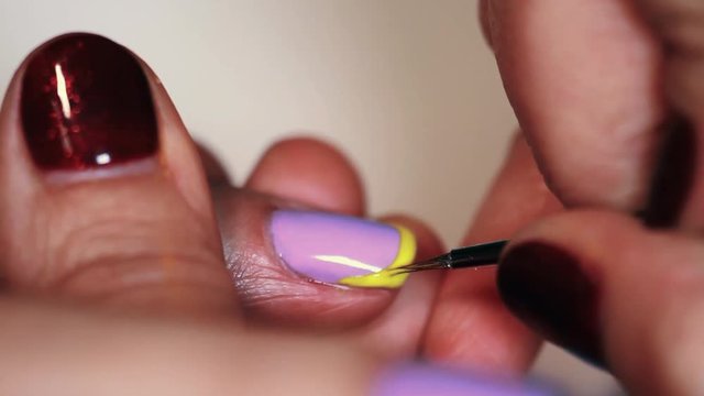 Manicure procedure woman hand drawing yellow stripe on purple finger nail polish, close up