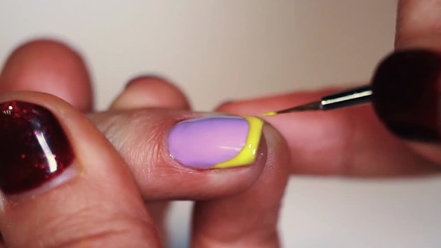 Manicure procedure female hand drawing yellow emoji on white finger nail polish, close up