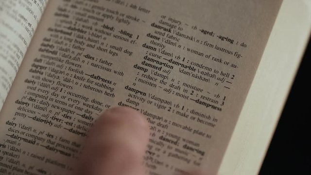 close up shot of Man looking for word by finger in English explanatory Dictionary on black background
