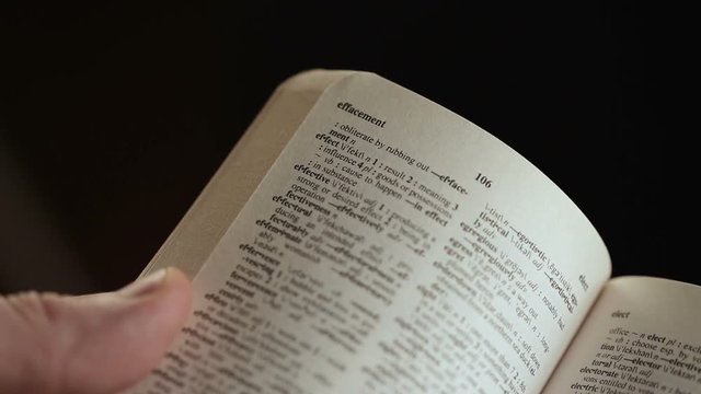 close up shot of Man looking for word by finger in English explanatory Dictionary on black background