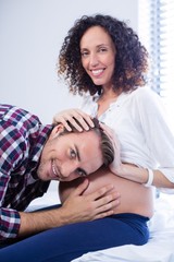 Fototapeta premium Smiling man listening to pregnant womans belly in ward