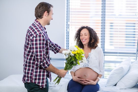 Man offering bunch of flowers to his pregnant woman in ward
