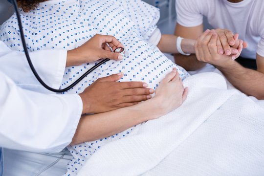 Doctor examining pregnant woman's belly with stethoscope in ward