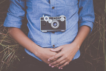 Young hipster woman with vintage camera lying down in field.