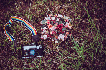 Naklejka premium Vintage camera with bouquet of flowers on grass background.
