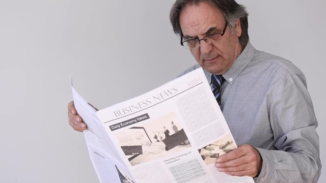 Senior man reading newspaper on gray background