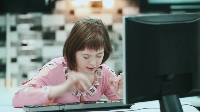 Girl with Down syndrome sitting at a computer at home and typing text.