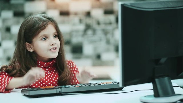 Little schoolgirl with dark hair and a blouse with polka dots, work at home computer, typing text.