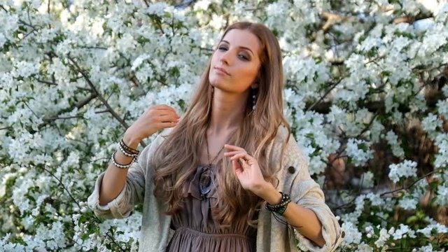 Beautiful young woman in long dress boho style under apple tree in blossom in Spring garden
