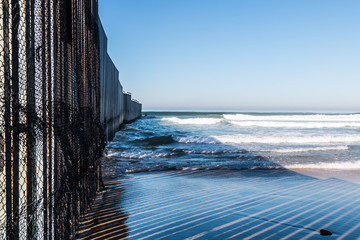 Close-up view of the international border wall extending out into the ocean between San Diego,...