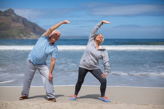 Senior couple doing stretching exercise on the beach - Powered by Adobe