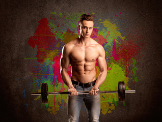 Fototapeta na wymiar Strong guy with colorful paint wall and weight