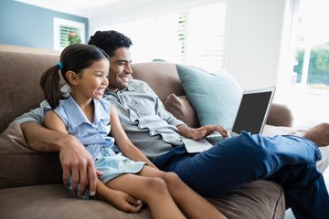 Father and daughter sitting on sofa and using laptop