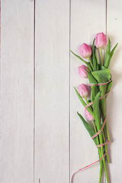 Background with bouquet of pink tulips and ribbon on white woode