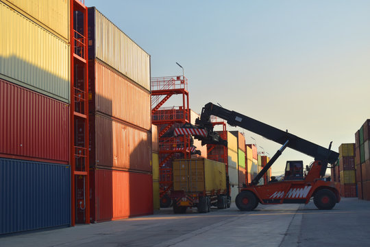 Container handling, reach stacker  lift off container from trailer inside container yard. Container logistics concept.