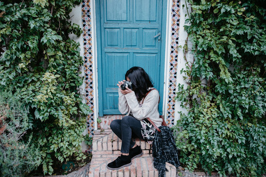 Young woman taking pictures sitting besides a blue door