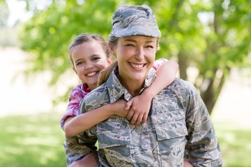 Female soldier giving a piggyback ride to her daughter in park