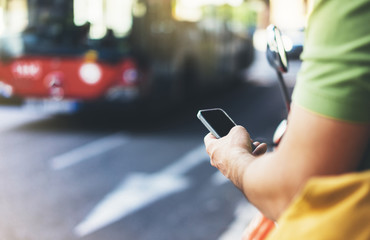 Man pointing on screen smartphone on background red bus, tourist hipster waiting taxi and using in hands mobile phone, traveler connect wifi internet, auto on backdrop city street, mockup station