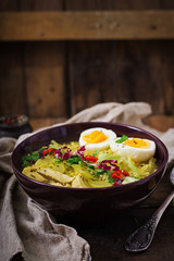 Noodle soup with chicken, celery and egg in a bowl on a old wooden background.
