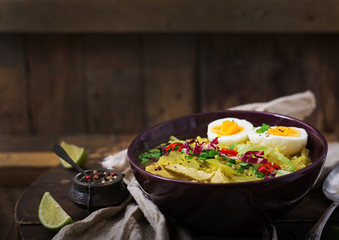 Noodle soup with chicken, celery and egg in a bowl on a old wooden background.