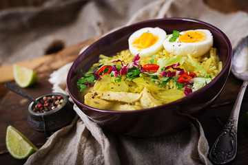Noodle soup with chicken, celery and egg in a bowl on a old wooden background.