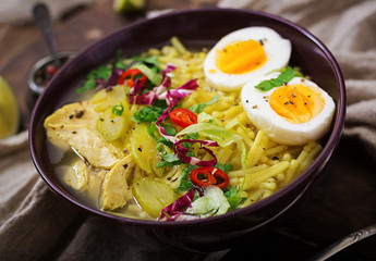 Noodle soup with chicken, celery and egg in a bowl on a old wooden background.