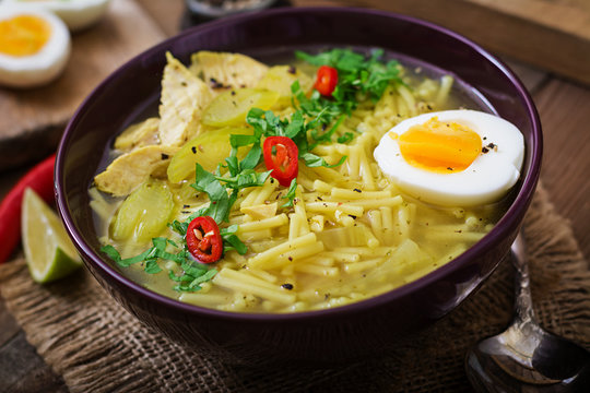 Noodle soup with chicken, celery and egg in a bowl on a old wooden background.