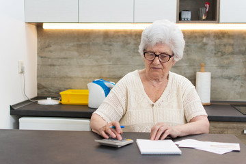 Senior woman with calculator and papers counting at home.