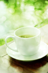 cup of coffee on wooden table with green garden bokeh.