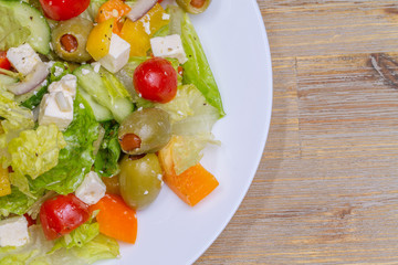 Greek salad in white glass dish plate, closeup from the top. Olives, tomatoes, paprika, bell pepper, cucumber, onion, feta cheese, olive oil. Standing at wooden background macro.