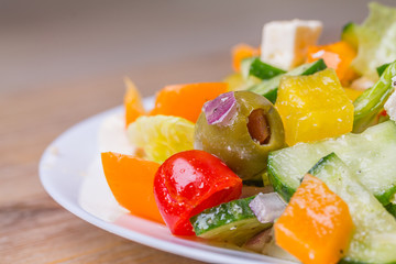 Fresh greek salad in white glass dish plate, closeup from side. Olives, tomatoes, paprika, bell pepper, cucumber, onion, feta cheese, olive oil. Standing at wooden background macro. Vegeterian food.