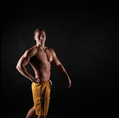 Fototapeta na wymiar Bodybuilder pose. Dark concept of fitness man. Sport life results. Strong person posing and look to the camera.