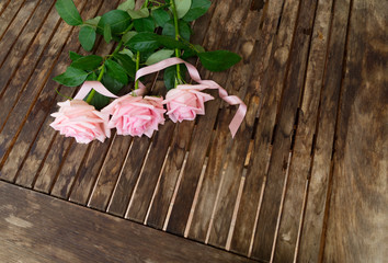 Pink blooming roses and silk ribbon on aged wooden table with copy space