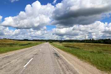 Fototapeta premium Landstraße unter blauem Himmel mit Turmwolken in Lettland