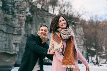 Obraz premium Beautiful pair of young people riding on the ice on the frozen lake among high rocks. They have a winter love story