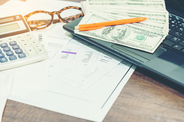 Finance concept : The United States hundred-dollar bills , calculator , bills ,eyeglasses , pen and laptop on the table 