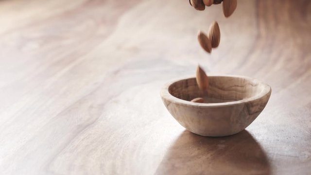 almonds falling in wood bowl on wooden table in slow motion, 180fps prores footage