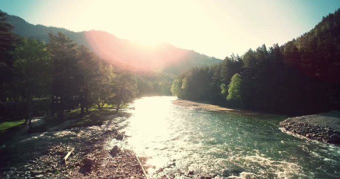 4k (UHD) aerial view. Low flight over fresh cold mountain river at sunny summer morning. Green trees and sun rays on horisont.