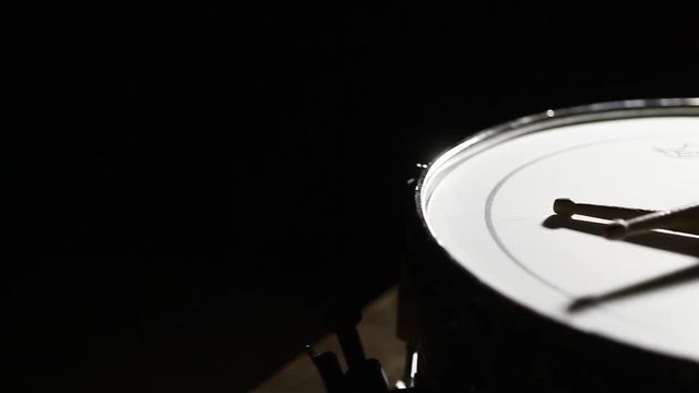Dolly shot of a snare drum and a pair of drumsticks.