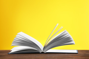 Opened book on wooden table and yellow background