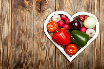 Vegetables. Peppers, tomatoes, garlic, onions, and radishes in the heart on rustic background