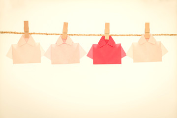 One Red among white origami shirt paper hanging  on rope