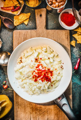 Spicy food cooking preparation. Frying pan with cut onion, garlic and chili on rustic cutting board with spices ingredients, top view. Mexican cuisine