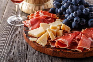 Prosciutto, wine, grape, parmesan on wooden table.