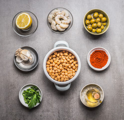 Bowls with Chickpeas salad ingredients: cooked Chickpeas, olives, shrimps, lemon, Paprika powder, herbs,olives oil on gray concrete background, top view, flat lay