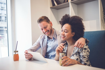 Happy middle age interracial couple sitting in cafe bar, smiling and looking at white tablet.
