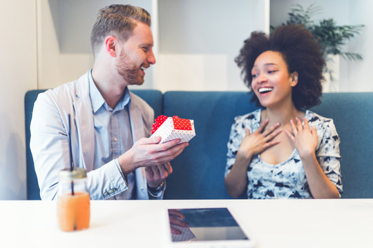 Happy middle age interracial couple sitting in cafe bar. Man giving Valentine's day gift to his girlfriend or wife. 