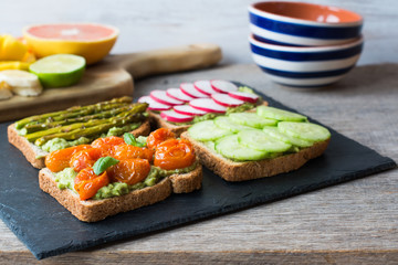 Selection of vegetarian toasts sandwiches made with baked tomoatoes, cucumbers,  asparagus, radish, blackberries on the black platter, selective focus