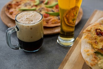 A mug of beer and glass with pizza in the background
