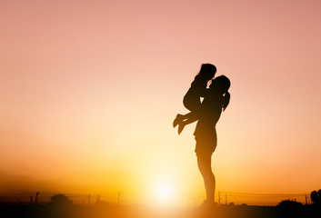 Silhouettes of mother and daughter playing at sunset evening sky background.